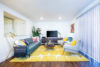 Lounge area blue couch 2 comfy grey chairs and coffee table on bright yellow rug.