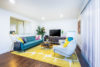 Lounge area blue couch 2 comfy grey chairs and coffee table on bright yellow rug.