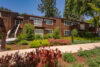 two story buildings with balconies green shrubs and mature trees provide some shade