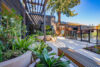 Outdoor patio with gray sectional seating, Contemporary metal pergola providing partial shade, Floor-to-ceiling glass windows on modern building