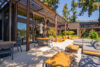 Covered outdoor patio with wooden pergola structure Gray sectional sofa and dining table with chairs Large planters with plants and modern wood-sided building