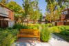 Wooden bench on concrete patio with ornamental grasses Multi-story townhouses with wood shingle siding and balconies mature trees and landscaped garden area between buildings